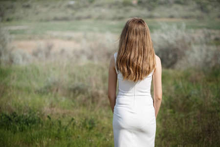 girl with beautiful hair is standing with her back in the field, sad girlの写真素材