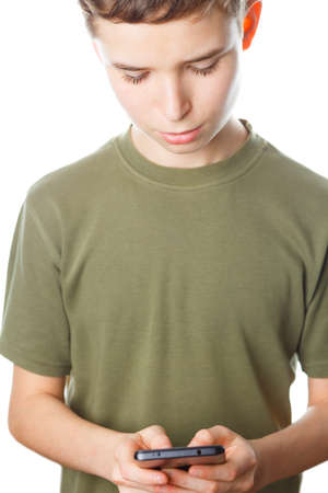 Teenager on isolated white background holds phone in his hands and writes a message. Child looking...