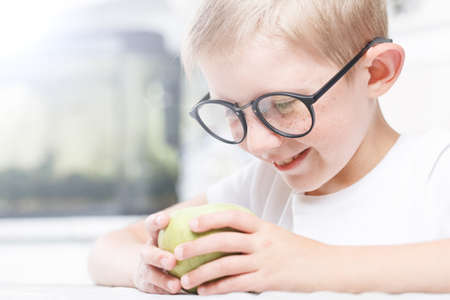 little boy in the kitchen, the child at breakfast chooses fruit, looks at the green apple
