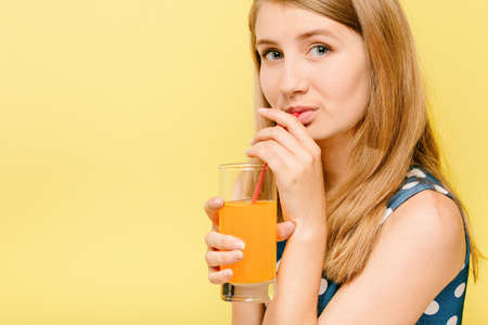girl in a pea dress on a yellow background drinking orange juice from a straw, model in a studio on...