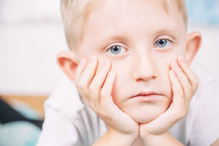little boy put his chin on his hands, the child looks at the cameraの写真素材
