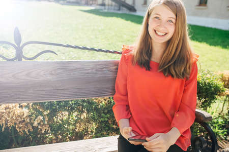 beautiful teenage girl with a backpack correspond with friends in social networks through a smartphone, a girl travels through Europe on a sunny dayの写真素材