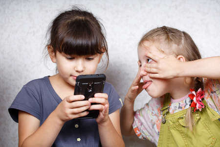 Children play on the mobile phone in games, an enthusiastic group of friends watch a cartoon on a tabletの写真素材