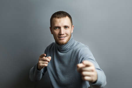Smiling man shows the index fingers of both hands at the camera. On a gray background.の写真素材