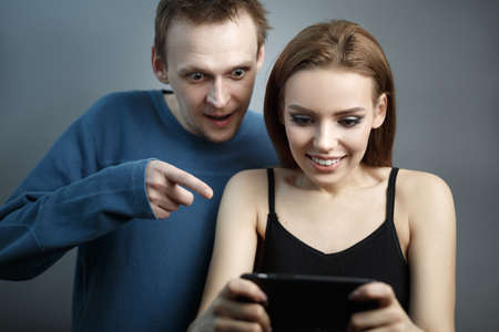Man with the girl excitedly looking at the smartphone. Are in an agitated state. Emotions of...