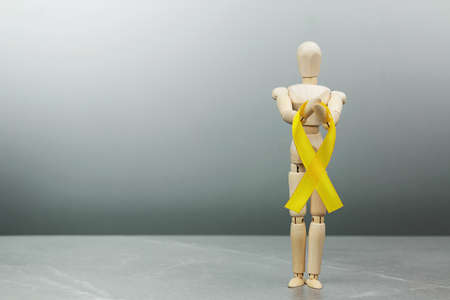 Wooden mannequin doll holds gold Childhood cancer ribbon on gray background. Cancer Control Concept. Symbolizing the day of AID, bladder, sarcoma and bone cancer.の写真素材