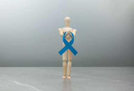 Wooden figure mannequin with blue prostate cancer ribbon on gray background. Cancer Control Concept. dark blue ribbon colon cancer symbol.の写真素材