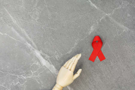Wooden hand with AID red ribbon in it, on gray marble isolated background. Cancer Control Concept....