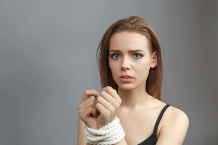 Young woman with tied hands on gray background studio photo Concept of violent action Human trafficking Kidnappingの写真素材