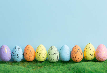 Row colored eggs on green grass with a blue background. Easter holiday.  Spring nature concept.