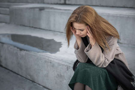 Sad beautiful woman in a bad mood sits on a granite bench on the street.の写真素材
