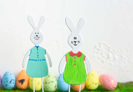 Pair of wooden toy bunny rabbits with row of colored eggs in green grass on white grunge background....