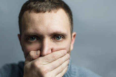 Man covered his mouth with his hand. Concept of silence. Say nothing. Be quiet. Studio photo on gray...