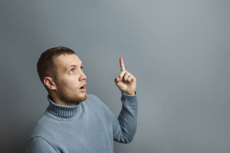 Man shows thumb up in surprise. Excited facial expression. Studio photo on a gray background.