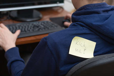 Man working at a computer with a note attached to his back. Kick me. April Fools day joke. Close up...