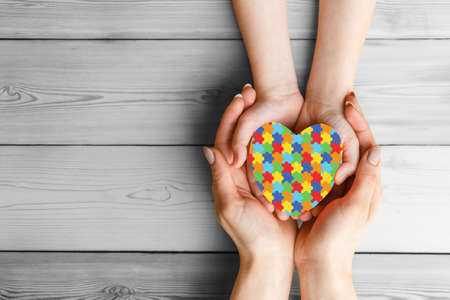 mental health care concept with puzzle or jigsaw pattern on heart Female hands hold childrens palms with a red heart in them. The concept of family love and support. World Autism Awareness dayの写真素材