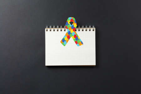 jigsaw pattern ribbon on open notebook isolated on black background, mental health care concept....