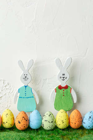 Pair of wooden toy bunny rabbits with row of colored eggs in green grass on white grunge background....