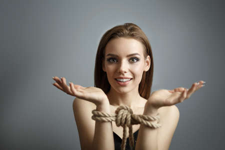 Smiling girl with tied hands with a rope on gray background.  Concept of Role playing game Shibari art on gray background Studio photoの写真素材