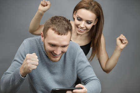 Man with the girl excitedly looking at the smartphone on gray isolated background in an agitated...