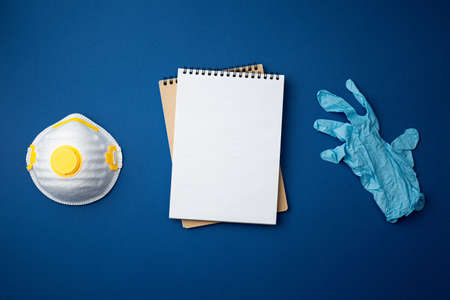 Spiral notebook with protective respiratory face mask and surgical gloves on blue background. Medic table top view concept.  Close up photo.の写真素材
