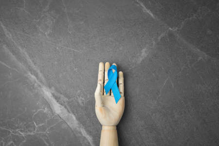 Wooden hand holds blue ribbon. Cancer Control Concept. Prostate Day. On a gray marble isolated background.の写真素材