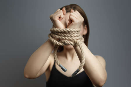 Woman with tied hands with the rope on gray background studio photo. Concept of violent action Human trafficking Kidnappingの写真素材