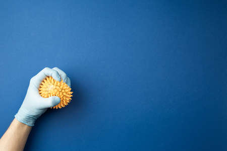 Hand in a medical glove studies the mock up of a virus on a blue isolated background. Pandemic Control Concept.の写真素材