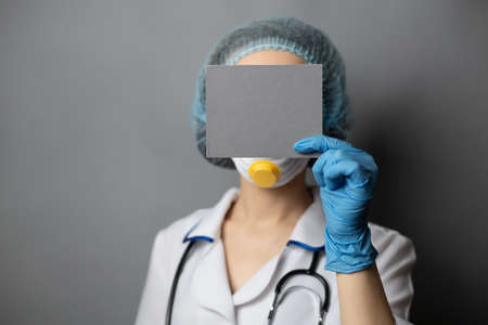 nurse showing a blank paper sheet in front of her head standing on a gray background in a dressing robe and gloves. the fight against the virus. The concept of coronavirus, HIV or cancer. Stop AIDS.の写真素材