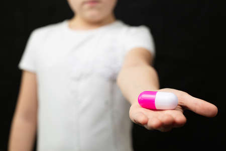 Girl in a white T-shirt holds an enlarged model of a pill in her palm on a black isolated background.の写真素材