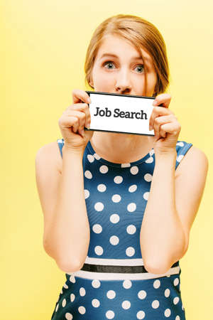 Surprised girl in sundress on a yellow isolated background. Holds in front smartphone with the inscription job search. Recruitment Idea of hiring and searching for human resources. Employment concept.の写真素材