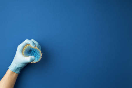 hand in medical gloves squeezes the virus on blue isolated background. Pandemic Control Concept....