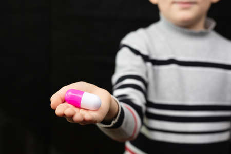 Boy in a gray sweater holds an enlarged model of a tablet in his palm on a black isolated background.の写真素材