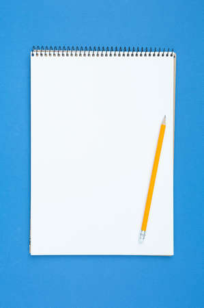 Spiral notebook and pencil with an eraser on a blue isolated background. Design concept with copy...