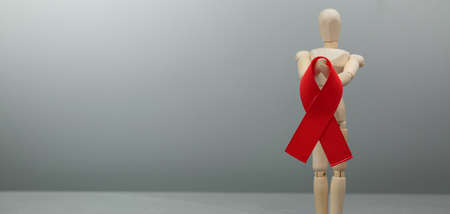 Wooden mannequin with HIV red ribbon. Cancer Control Concept. Symbolizing the day of AIDS. On a gray background.の写真素材