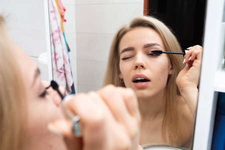 Beautiful woman with long blond hair in the bathroom in a white bath towel looks in the mirror....