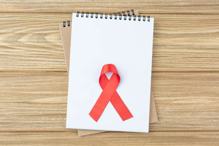 Open notebook with red AIDS ribbon on wooden table. copy space for notes. Cancer Day, HIV concept. Flat lay notepad.の写真素材