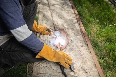 The welder is engaged in electric welding on the open air on a background of green grass.