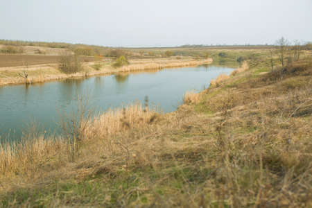 River channel in the countryside with last years yellow grass along the banks. The beginning of...