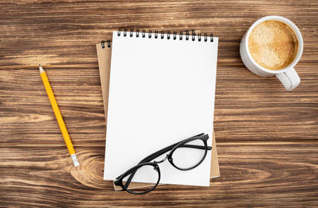 Spiral notebook with pencil, glasses and coffee cup on a wooden background. Design concept with copy space for notes. Blank page for business text. Office notepad. Top view.の写真素材
