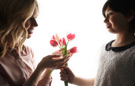 Beautiful woman and little boy with a bouquet of tulips. A child gives flowers to mom. White...