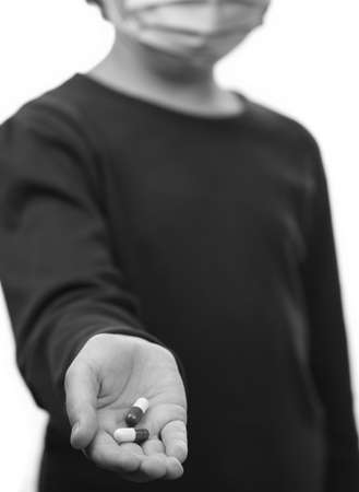 Little girl in medical mask holds pills on white isolated background. Backlight vertical Photo. Healthcare and medical concept. Prevention of bacterial infection coronavirus or Covid 19.の写真素材