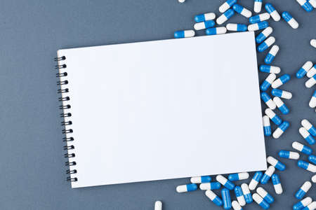 Open spiral notebook with clear page and capsule pills on blue background. Design business, medicine supplies or medical concept. Ready for adding or mock up. Top view.の写真素材