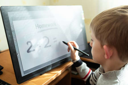 Little boy do homework on a graphic tablet at home. Remote Education Concept. Distance schooling...