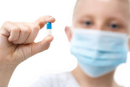 Little boy in medical mask hold a pill on white isolated background. Backlight Photo. Healthcare and medical concept. Prevention of virus infection coronavirus or Covid 19.の写真素材
