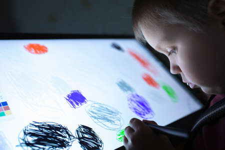 Little boy draw on a graphic tablet in the evening in a dark room under the light of the monitor. Creative education concept. Close up view.の写真素材