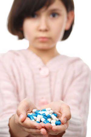 Little girl holds handful of pills on white isolated background. Backlight vertical Photo. Healthcare and medical concept. Prevention of bacterial infection coronavirus or Covid 19.の写真素材