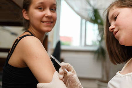 Girl helps her sister give an injection of insulin in a shoulder. Health care and medicine concept....