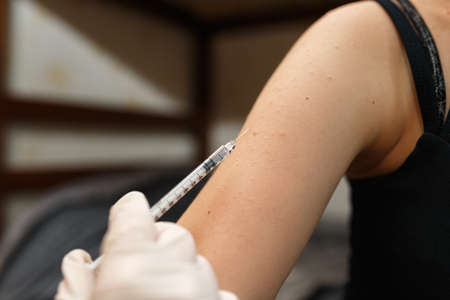 Young girl receiving vaccination immunisation by professional health worker, focus on shoulder....