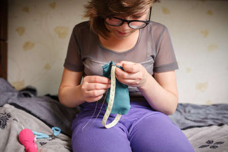Girl with glasses is engaged in needlework. Hobby sewing in free time, at home.の写真素材